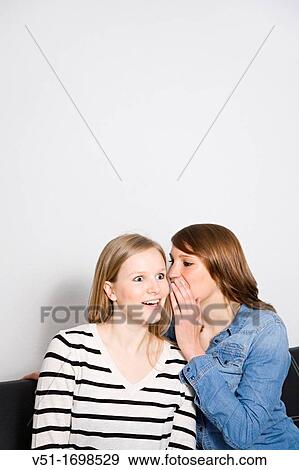 Blonde woman being told a secret by her friend on the couch View Large Photo Image Stock Photo - Blonde woman being told a secret by her friend on the couch. Fotosearch