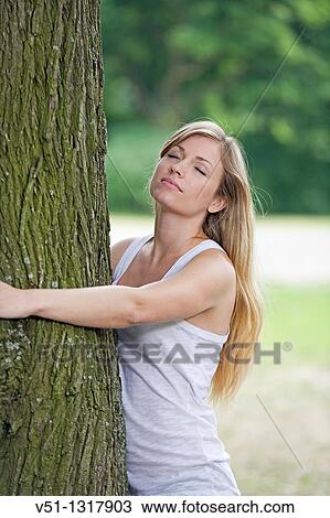 Stock Image - Blonde woman embracing a tree in the park. Fotosearch