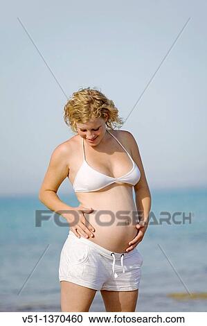 Stock Image - Blonde woman enjoying her pregnancy at the beach. Fotosearch