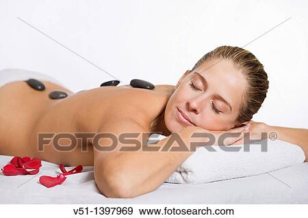 Stock Photo - Blonde woman in massage with stones und petals. Fotosearch