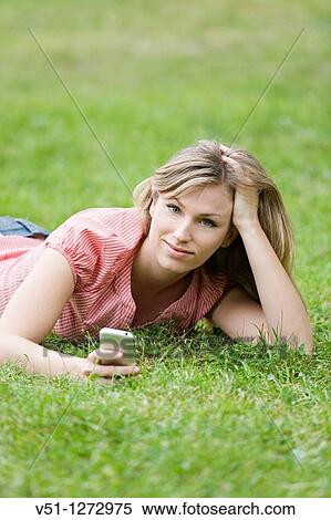 Stock Photography - Blonde woman lying down on the grass with mobile. Fotosearch