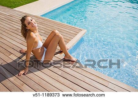 Stock Image - Blonde woman sitting by the pool and smiling at camera. Fotosearch