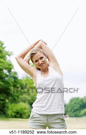 Stock Image - Blonde woman stretching in the park and smiling at camera. Fotosearch