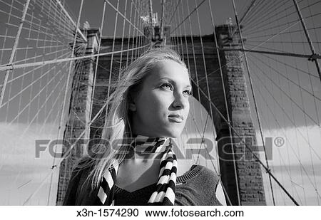 Stock Image - Blonde woman with Brooklyn Bridge, New York City, in Background. Fotosearch