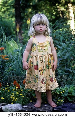 Picture - Blonde young girl, 3-4 years old, standing on rock wall in garden on a summer morning. Fotosearch
