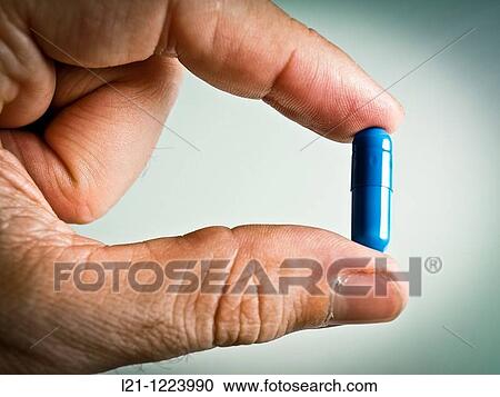 Stock Image - Blue pill between two fingers.. Fotosearch