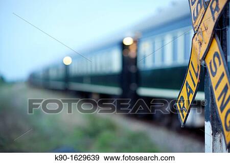 Blurred Rovos Rail passenger train passing by a Railroad Crossing, with the yellow warning sign about trains in the foreground, Southern Africa, Botswana View Large Photo Image Stock Photo - Blurred Rovos Rail passenger train passing by a Railroad Crossing, with the yellow warning sign about trains in the foreground, Southern Africa, Botswana. Fotosearch