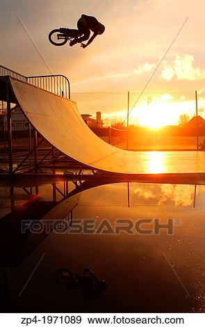 Stock Photo - BMXer riding a halfpipe in Swansea, South Wales during a sunset, rider silhouetted with his reflection in a puddle.. Fotosearch