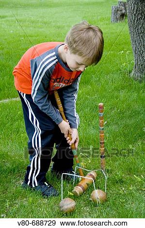 Stock Photo - Boy age 7 returning wooden ball through double croquet wickets with a long-handled mallet Clitherall Minnesota USA. Fotosearch