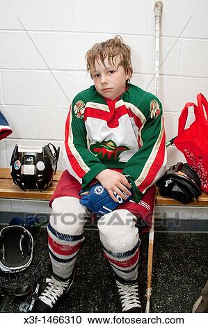 Stock Image - Boy age 8 in locker room wearing hockey uniform tired after a game St Paul Minnesota MN USA. Fotosearch