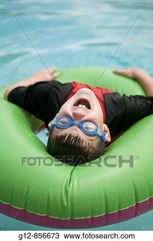 Stock Image - Boy, age 8, swims in pool with inflatable tube in Sedona, AZ.. Fotosearch
