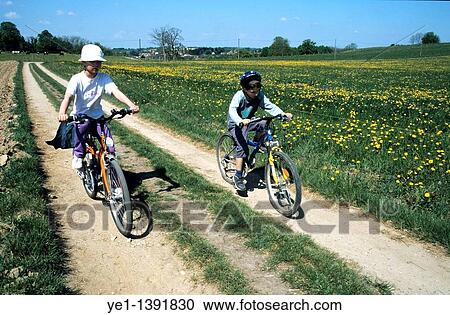 Boy and girl cycling on a dirt road together through the countryside View Large Photo Image Stock Image - Boy and girl cycling on a dirt road together through the countryside. Fotosearch