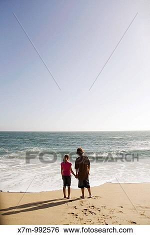 Boy and girl looking out contemplatively at the vast ocean as the sun begins to set View Large Photo Image Stock Photograph - Boy and girl looking out contemplatively at the vast ocean as the sun begins to set. Fotosearch