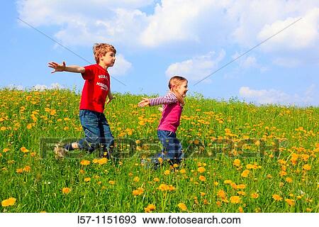 Stock Image - boy and girl running through field of Dandelions, Zuercher Oberland, Zuerich, Switzerland. Fotosearch