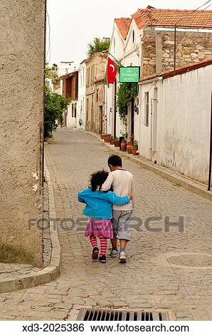 Stock Photograph - Boy and girl walking in old street with arms around each other, Bozcaada, Turkey. Fotosearch