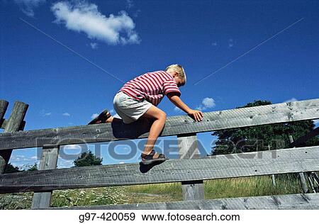 Stock Photo - Boy climbing over a fence.. Fotosearch
