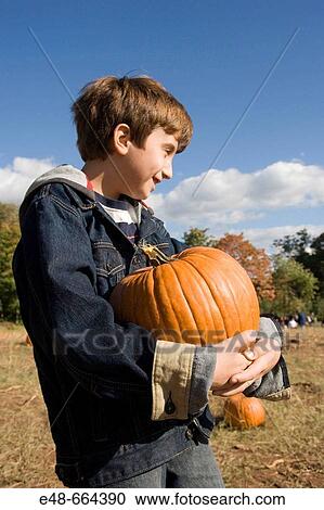 Stock Image - Boy holding pumpkin in pumpkin patch. Fotosearch