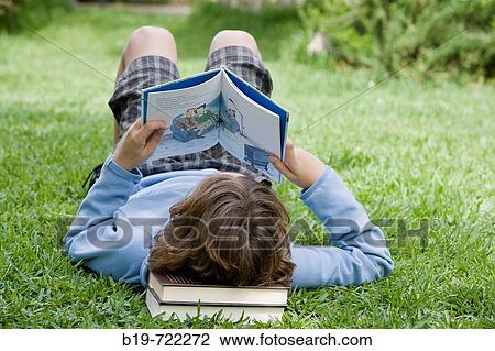 Boy laying on grass reading a book View Large Photo Image Stock Image - Boy laying on grass reading a book. Fotosearch