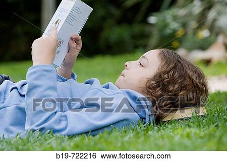 Stock Photograph - Boy laying on grass reading a book. Fotosearch