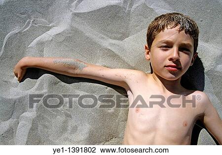 Stock Image - Boy lying on a sandy beach, Camargue, France. Fotosearch
