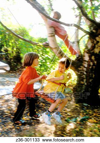 Stock Image - Boy on seesaw with girl pushing and another girl on tree. Fotosearch