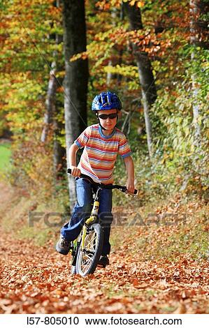 Stock Image - boy riding his bicycle on road with leaves in fall, autumn foliage covering path in forest, autumn, fall, Zuerich, Switzerland. Fotosearch
