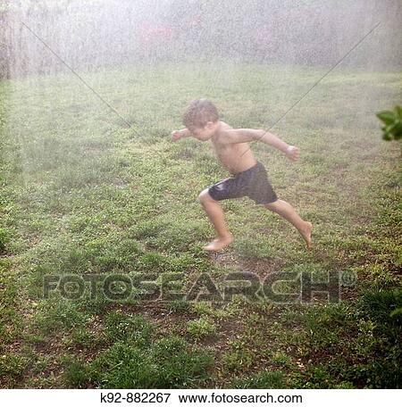 Boy running through a sprinkler outside in his backyard on a warm day. View Large Photo Image Stock Photo - Boy running through a sprinkler outside in his backyard on a warm day.. Fotosearch