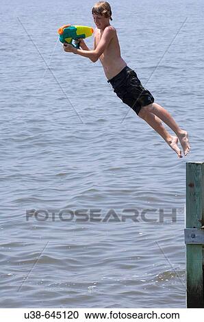 Stock Image - boy shooting water gun while jumping into the Albemarle Sound,. North Carolina. Fotosearch
