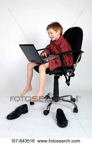 Stock Photograph - boy sitting on black office chair, wearing grown up red business shirt, with laptop on his lap, laughing, white background, Studio, Switzerland. Fotosearch