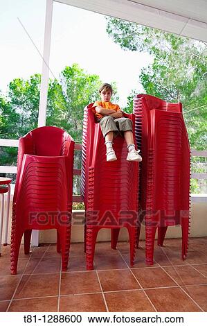 Boy sitting on stacked chairs View Large Photo Image Stock Image - Boy sitting on stacked chairs. Fotosearch