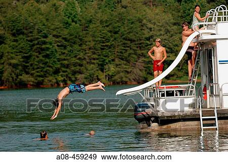 Stock Photo - Boy slides headfirst from sliding board off back of houseboat as others kids watch. Location: Smith Mountain Lake, Virginia, USA. Fotosearch