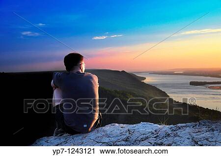 Stock Image - Boy watches sunset skies in Russian National Park sitting on a steep rock of Zhiguli mountains. Fotosearch