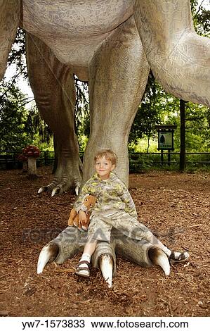 Stock Image - Boy with his teddy lion sitting on a leg of a dinosaur. Fotosearch