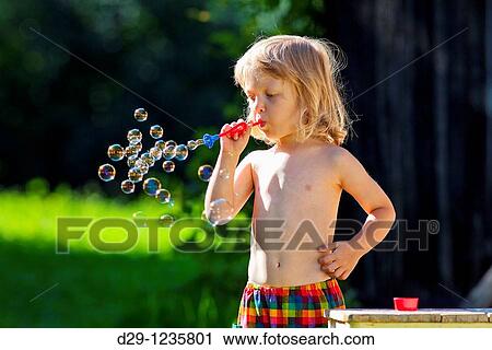 Stock Image - boy with long blond hair blowing soap bubbles. Fotosearch
