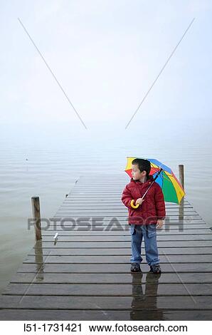Stock Image - boy with multicoloured umbrella under the raoin by a lake, Albufera de Valencia Nature reserve, Valencia, Spain. Fotosearch