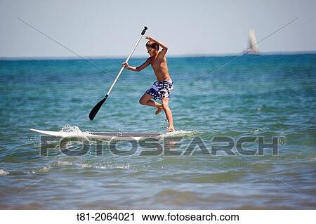 Stock Image - Boy with surfboard paddling about in the Mediterranean Sea, Benicassim, Castellon province, Comunidad Valenciana, Spain. Fotosearch