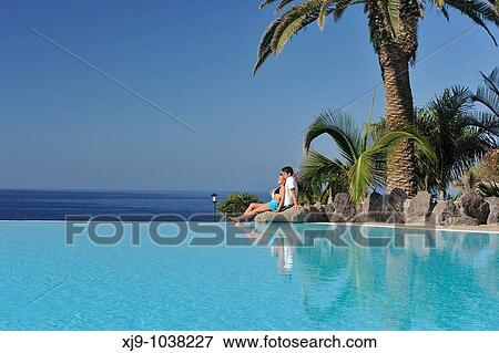 Stock Photo - Boys and girls sat facing the sea and pool. Fotosearch