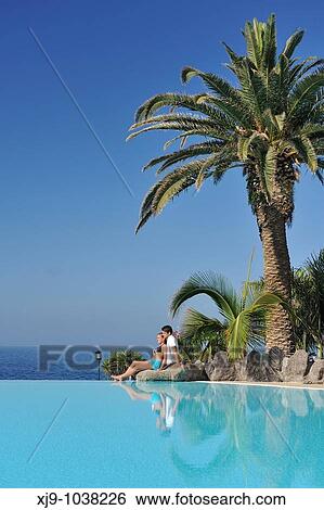 Stock Photograph - Boys and girls sat facing the sea and pool. Fotosearch