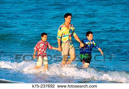Stock Image - Boys walking through the waves with dad. Fotosearch