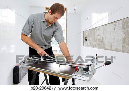 Stock Photo - Bricklayer cutting tile. Manual tile cutter. Construction Industry.. Fotosearch