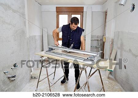 Stock Photo - Bricklayer cutting tile. Manual tile cutter. Kitchen renovation work. Construction Industry.. Fotosearch