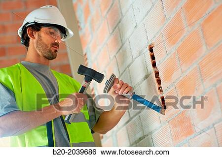 Stock Photograph - Bricklayer making a groove in the brick wall to place electrical wires. Hammer and chisel hand tools. Construction. Building work. Donostia. San Sebastian. Gipuzkoa. Basque Country. Spain.. Fotosearch