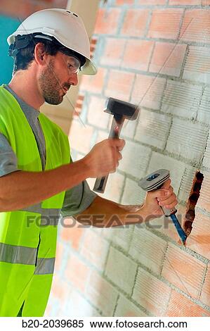 Stock Photography - Bricklayer making a groove in the brick wall to place electrical wires. Hammer and chisel hand tools. Construction. Building work. Donostia. San Sebastian. Gipuzkoa. Basque Country. Spain.. Fotosearch