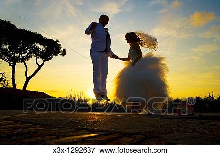 Stock Photo - Bride and groom jumping for joy at sunset. Fotosearch