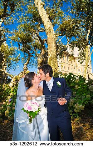Stock Image - Bride and groom kissing in a park. Fotosearch