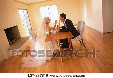 Stock Photo - Bride and groom sharing a bowl of spaghetti sitting in new home with no furniture. Fotosearch