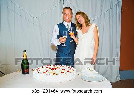 Picture - Bride and groom toasting in front of wedding cake. Fotosearch
