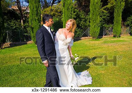Stock Photograph - Bride and groom walking through a park. Fotosearch