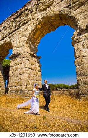 Bride and groom walking together in under ancient aqueduct roman ruins in Rome Italy View Large Photo Image Stock Photo - Bride and groom walking together in under ancient aqueduct roman ruins in Rome Italy. Fotosearch