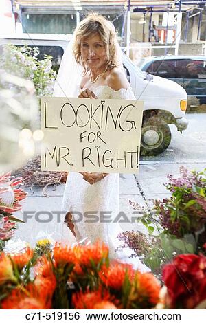 Bride holding sign? Looking for Mr. Right? in front of a flower shop View Large Photo Image Stock Photograph - Bride holding sign? Looking for Mr. Right? in front of a flower shop. Fotosearch